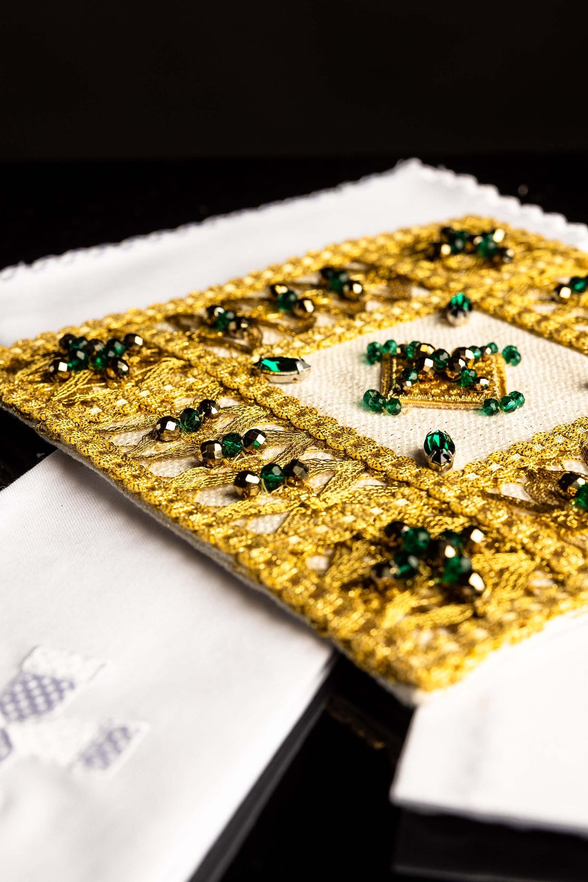 Kelchwäsche-Set, Nahaufnahme der goldenen Stickerei mit grünen Steinen und weißem Tuch