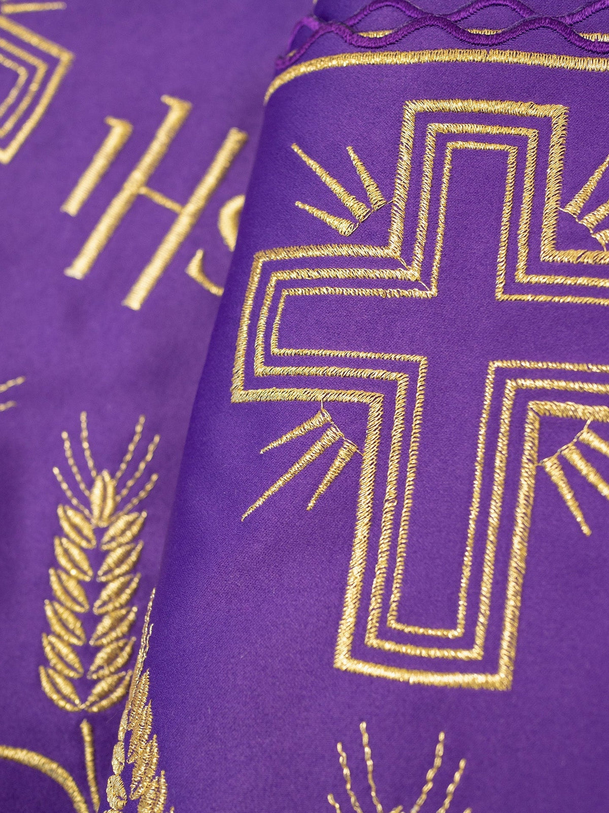 Meter mit IHS-Monogramm, Nahaufnahme der goldenen Kreuzstickerei auf violettem Stoff